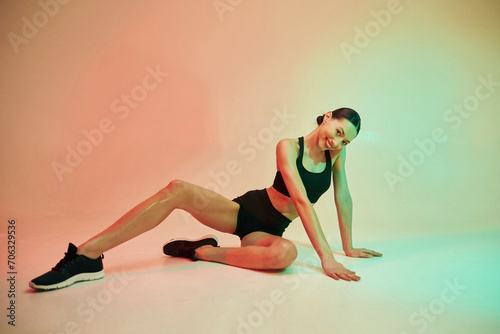 Against colorful background. Young fitness woman in sportive clothes in studio