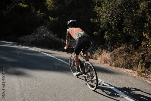 Man cyclist in full cycling kit riding a road bicycle on the mountain road Bernia, Costa Blanca, Alicante, Spain. Male professional cyclist climbing in the spanish mountains back view.