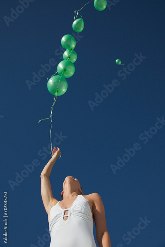 Woman releasing green balloons in a cloudless sky - low angle view
 photo