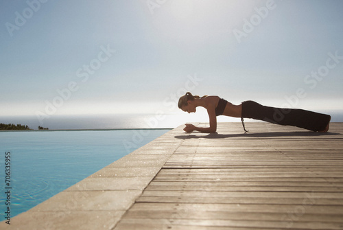 Young woman practicing yoga by a swimming pool with ocean in the background
 photo