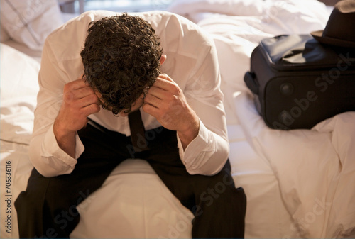 Businessman sitting on a bed with his head in his hands
