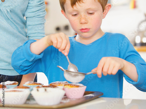 Young boy sprinkling cupcakes with icing sugar
