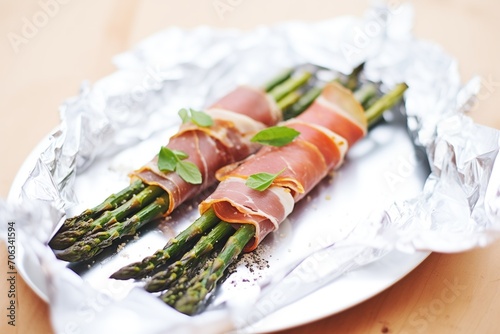 oven-roasted prosciutto-wrapped asparagus on a shiny aluminum foil sheet