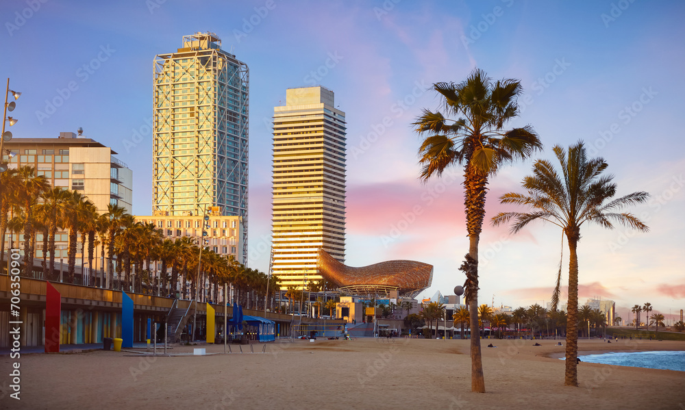 Barcelona, Spain. Panoramic view at Barceloneta Beach cityscape from sea. Sunset landscape with blue sky and palm trees on the beach. Sandy coastline. Popular touristic vacation destination.