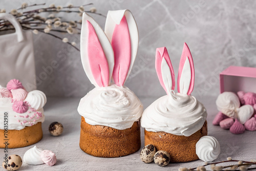 Beautiful stylish still life. Easter cake with rabbit  hare  ears  meringue  marshmallows  Easter eggs and willow branches and on a light concrete background. Happy Easter 2024.