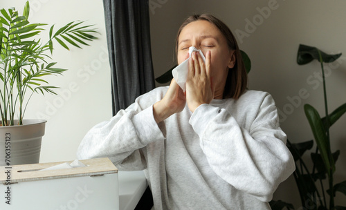 Sick unhealthy woman sneezes in paper tissue for cold, sinusitis, allergies or winter virus at home. Female with labial herpes virus on face caused by immune weakness seasonal colds, vitamins loss photo