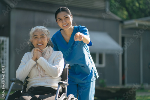 Smiling physiotherapist taking care of the happy senior patient in wheelchair, outdoor. photo
