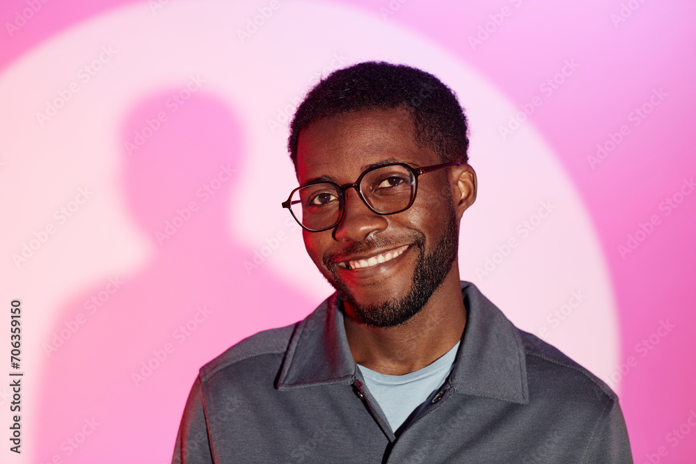 Medium close up shot of smiling bearded Black man in glasses standing at rich pink background and looking at camera Medium close up shot of smiling bearded Black man in glasses standing at rich pink background and looking at camera