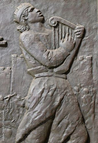 Bronze relief of a young man playing ancient harp while walking