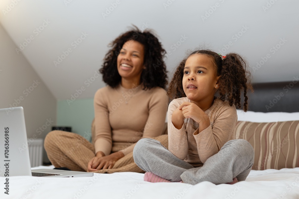 Happy african american woman and her little daughter watching TV