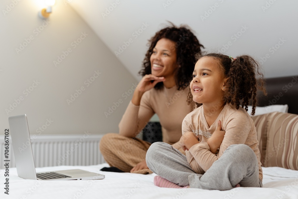 Happy african american woman and her little daughter watching TV