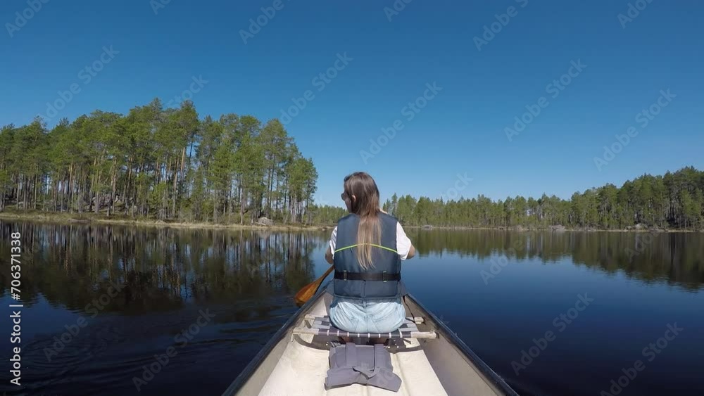 Woman paddling across a lake with birch trees. Woman paddling across a lake with birch trees.