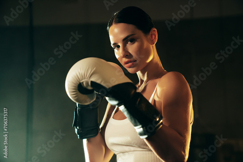 Cinematic portrait of sexy fighter woman in a boxing ring. Model wearing white gloves and braided hair. Hot confident female relax after training for fight match. Stands near the rope. In a smoke © halayalex