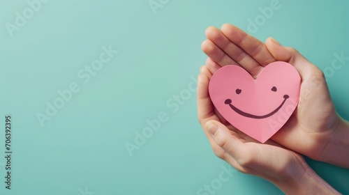 Hand Holding a Pink Paper Smile Symbolizing Emotional Mental Health and Love on a Blue Background, Top-down view, Heart-Shaped Smiley, Support Positivity, Wellness, and Happiness Concept