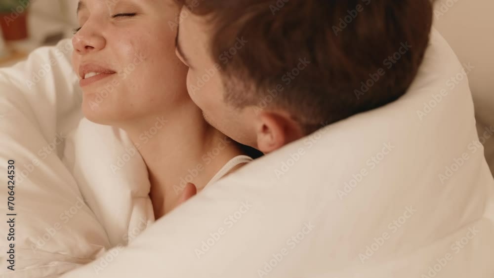 Сloseup shot of a young man kissing a beautiful woman on the cheek. Their eyes closed, covered in a white blanket, a moment of shared affection and bliss. Сloseup shot of a young man kissing a beautiful woman on the cheek. Their eyes closed, covered in a white blanket, a moment of shared affection and bliss.