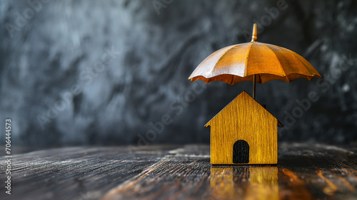 Small wooden house under an umbrella on the table, gray background, property insurance