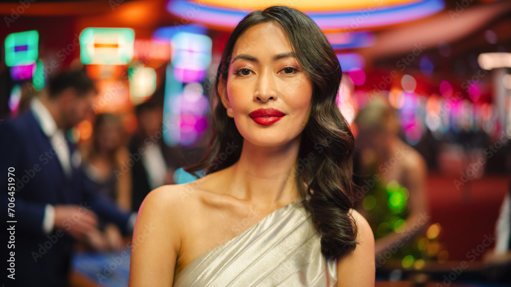 Beautiful Young Asian Woman Standing in a Glamorous Atmosphere of a Casino, Looking at Camera. Anonymous Gamblers Playing in the Background. Close Up Portrait