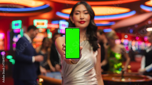 Modern Casino Setting: Gorgeous Asian Brunette Woman Posing with a Mobile Phone with a Green Screen Placeholder Space for Advertising or Commercial Materials for a Gambling Industry