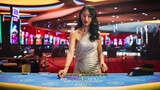 Portrait of a Beautiful Asian Female Croupier Dealing Playing Cards in a Casino for a Game of Baccarat. Card Dealer Looking at the Camera and Revealing Possibly Winning Combitnation. Winning Big
