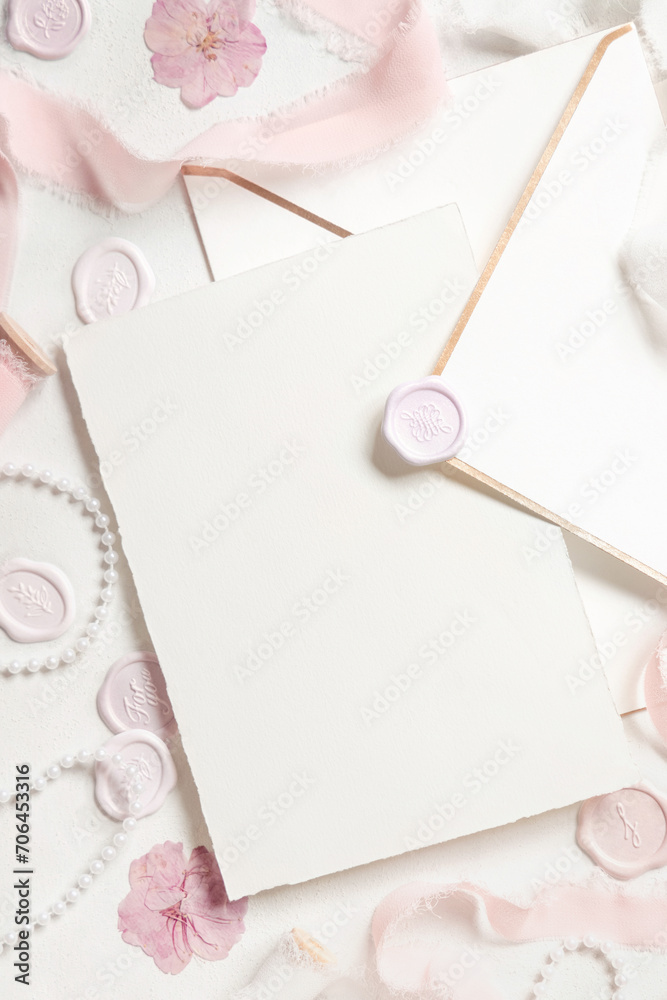 Card and envelope near pink decorations, seals and silk ribbons on white table top view, wedding mockup Card and envelope near pink decorations, seals and silk ribbons on white table top view, wedding mockup