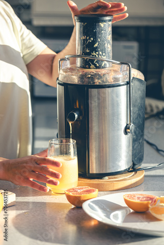 A woman makes orange juice at home in the kitchen with an electric juicer.