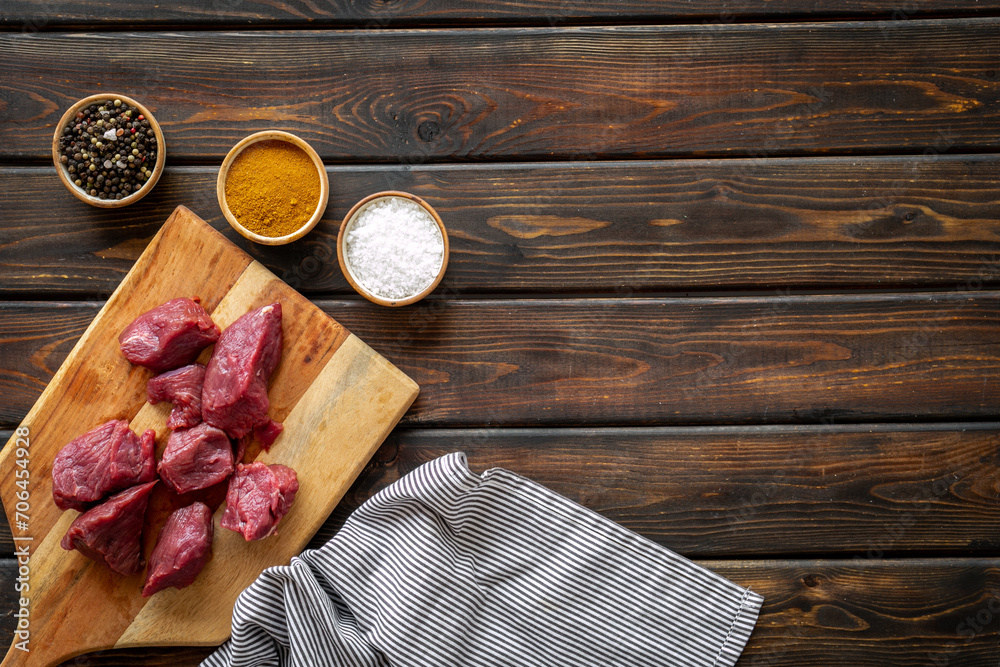 Raw beef meat cutting into pieces on wooden board with spices Raw beef meat cutting into pieces on wooden board with spices