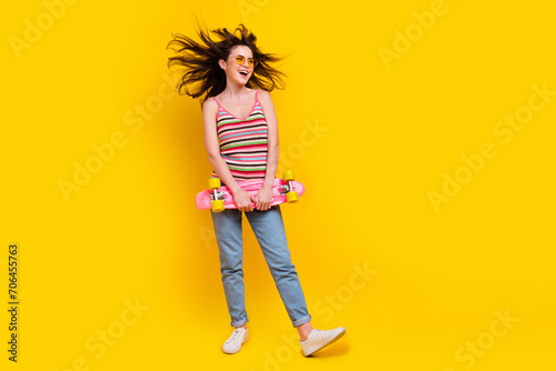 Full size photo of overjoyed woman dressed knitwear top hold skateboard look at promo empty space isolated on yellow color background photo