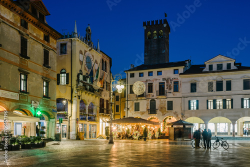 Bassano del Grappa, Italy - January 09, 2024: People Piazza Libertà in cafe tables in the evening in winter. On the left the town hall.