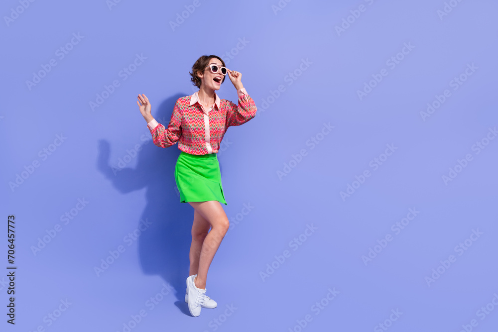 Full length photo of astonished girl touching sunglass wear green skirt look at discount empty space isolated on blue color background Full length photo of astonished girl touching sunglass wear green skirt look at discount empty space isolated on blue color background