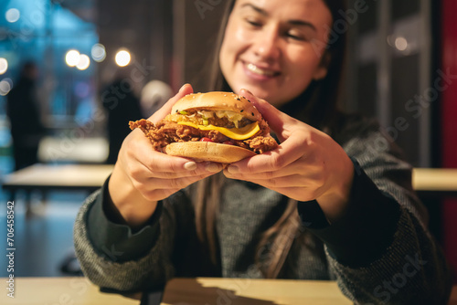 An appetizing chicken burger in female hands in a fast food restaurant.