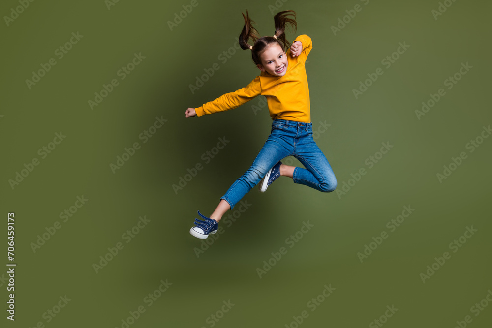 Full size photo of cute small kid with tails hair wear pullover flying clenching fists near empty space isolated on khaki color background