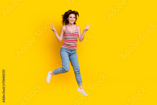 Full size photo of optimistic lovely woman dressed knit top jeans jumping showing v-sign isolated on vivid yellow color background