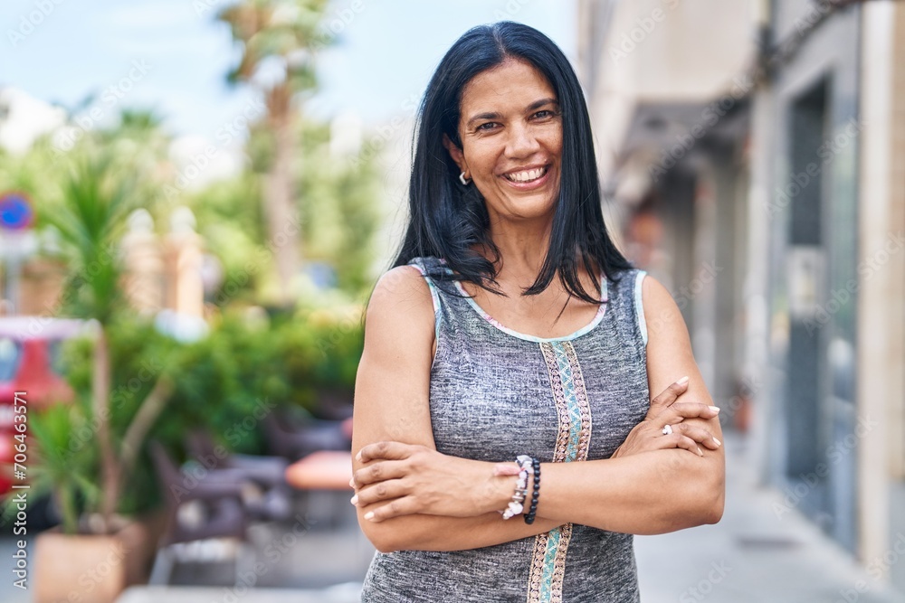 Middle age hispanic woman standing with arms crossed gesture at street