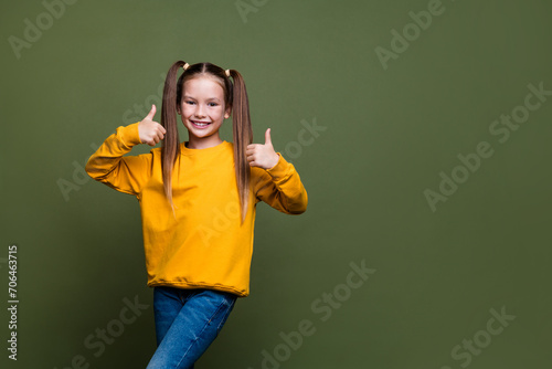Photo of good mood adorable schoolgirl with ponytails wear yellow pullover showing thumb up approve isolated on khaki color background © deagreez