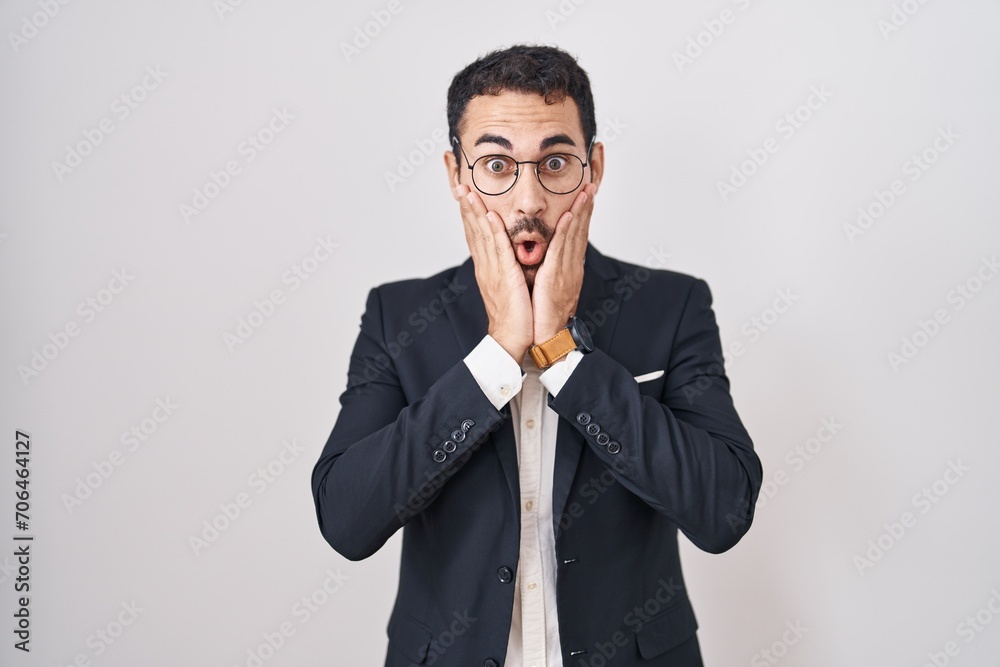 Handsome business hispanic man standing over white background afraid and shocked, surprise and amazed expression with hands on face Handsome business hispanic man standing over white background afraid and shocked, surprise and amazed expression with hands on face