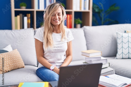 Young blonde woman studying using computer laptop at home winking looking at the camera with sexy expression, cheerful and happy face.