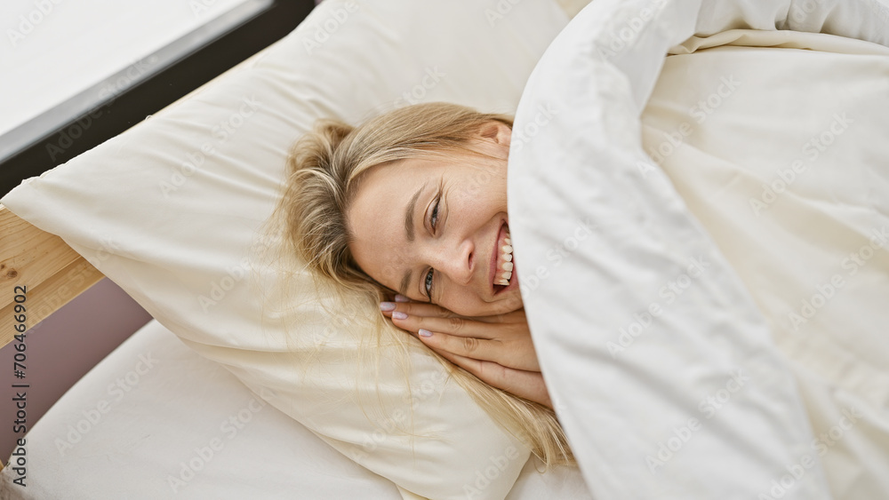 A joyful blonde woman lying in a cozy bedroom, exuding warmth and relaxation. A joyful blonde woman lying in a cozy bedroom, exuding warmth and relaxation.