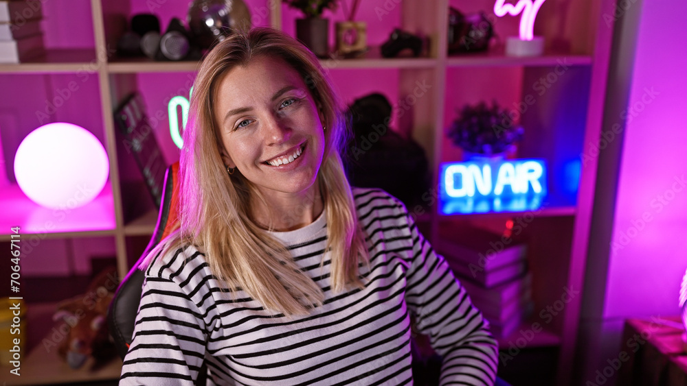A smiling blonde woman in a striped shirt poses in a vibrant gaming room with purple lighting at nighttime.