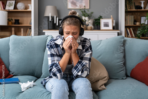 Young woman sitting at home listening to audio books or podcast on wireless headphones and crying. She feels sad and depressed about the subject they talking about.