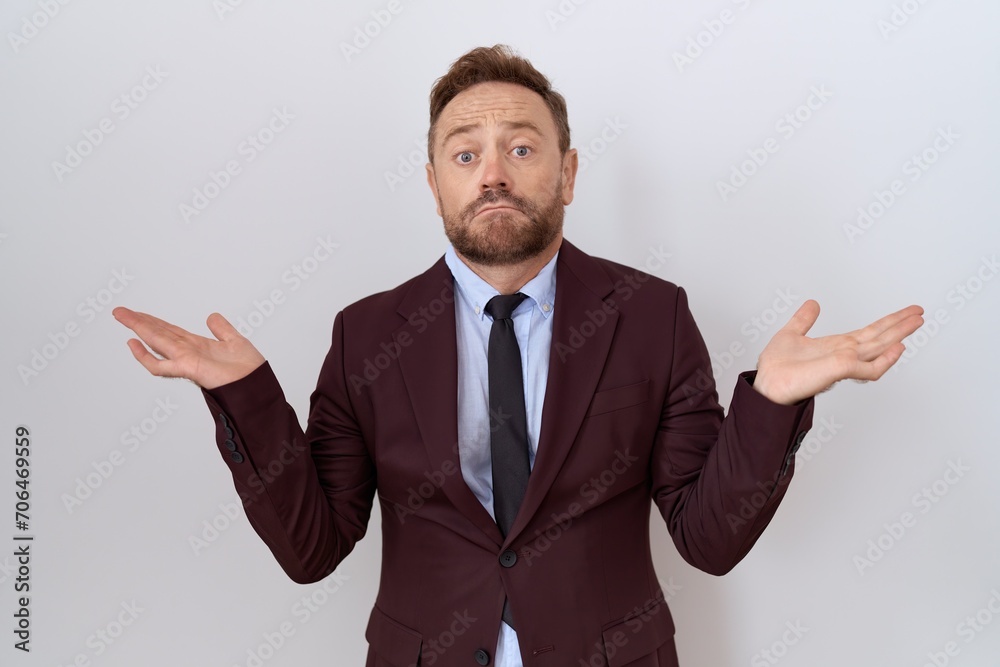 Middle age business man with beard wearing suit and tie clueless and confused expression with arms and hands raised. doubt concept. Middle age business man with beard wearing suit and tie clueless and confused expression with arms and hands raised. doubt concept.