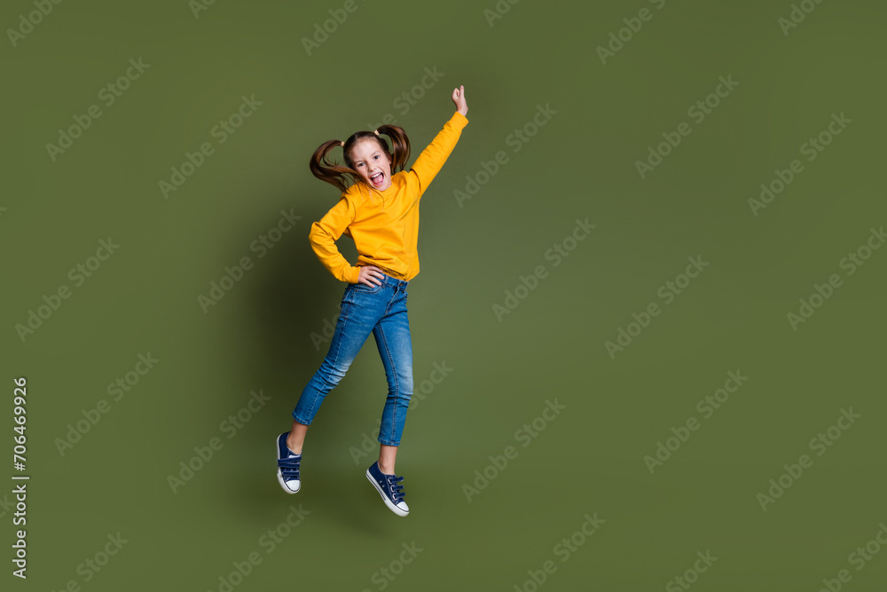 Full size photo of optimistic small kid with tails hair wear yellow pullover flying hold fist up isolated on khaki color background