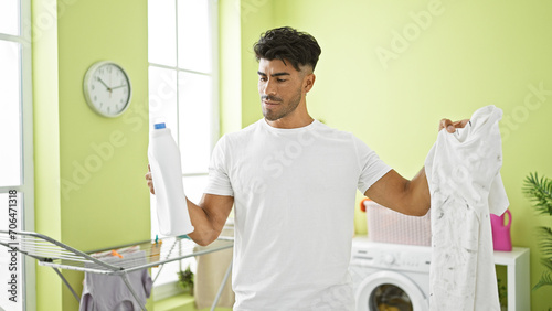 Handsome hispanic man evaluates laundry results with detergent in a bright, green room.