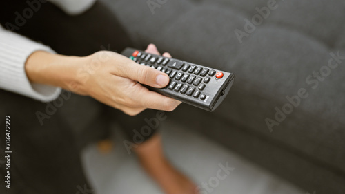 A close-up of a woman's hand holding a television remote control, portraying leisure time at home.