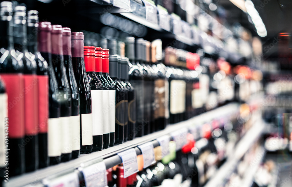 Liquor store, alcohol shop. Red wine on shelf. Focus on bottles, supermarket aisle in background. Alcoholic drink sale and selection in grocery market. Pinot noir, merlot or sauvignon cabernet. - obrazy, fototapety, plakaty 