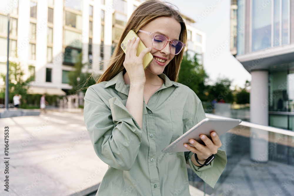 Businesswoman multitasking with a tablet and phone call outdoors, smiling in urban setting. Businesswoman multitasking with a tablet and phone call outdoors, smiling in urban setting.