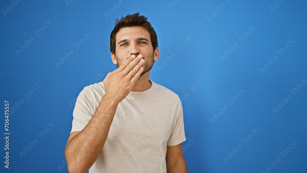 Handsome young hispanic man covering mouth against blue outdoor background. Handsome young hispanic man covering mouth against blue outdoor background.
