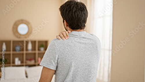 Rear view of a young man with a shoulder pain in a modern living room. photo