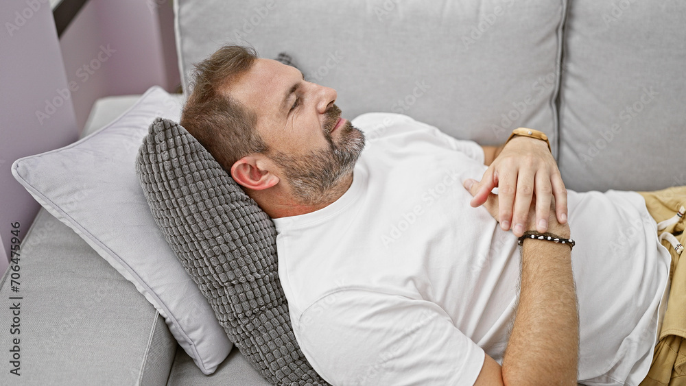 Fototapeta premium Handsome mature hispanic man with grey hair relaxing on a sofa indoors at home.