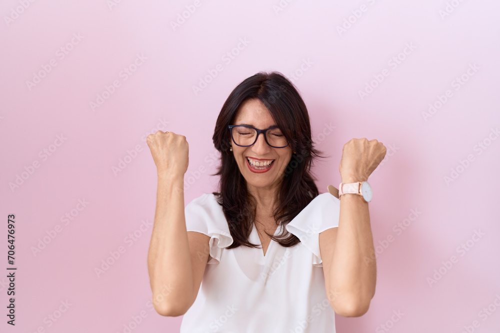 Middle age hispanic woman wearing casual white t shirt and glasses celebrating surprised and amazed for success with arms raised and eyes closed. winner concept. Middle age hispanic woman wearing casual white t shirt and glasses celebrating surprised and amazed for success with arms raised and eyes closed. winner concept.