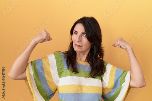 Middle age hispanic woman standing over yellow background showing arms muscles smiling proud. fitness concept.